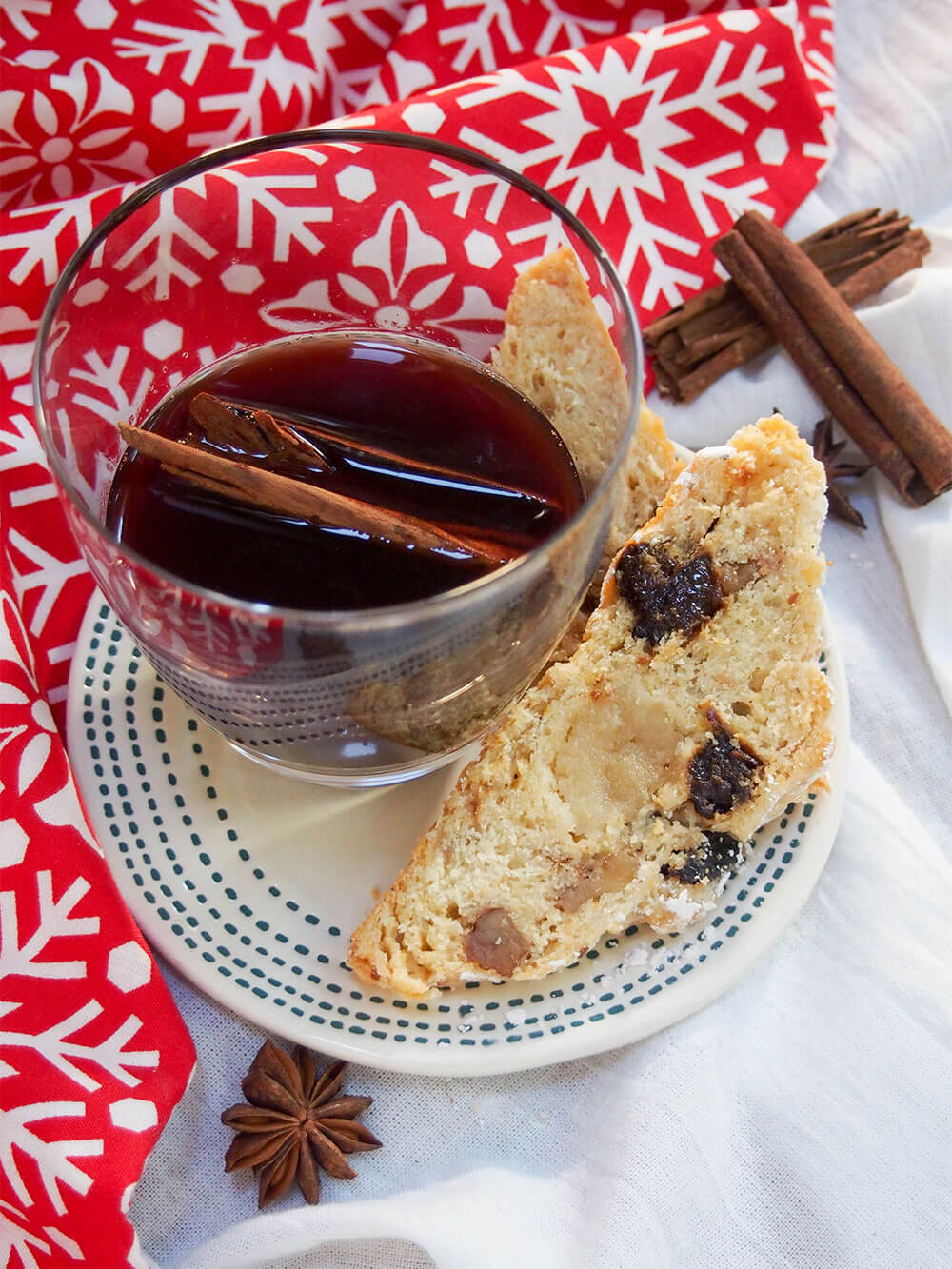 slice of stollen with a glass of gluhwein on small plate with cinnamon sticks behind