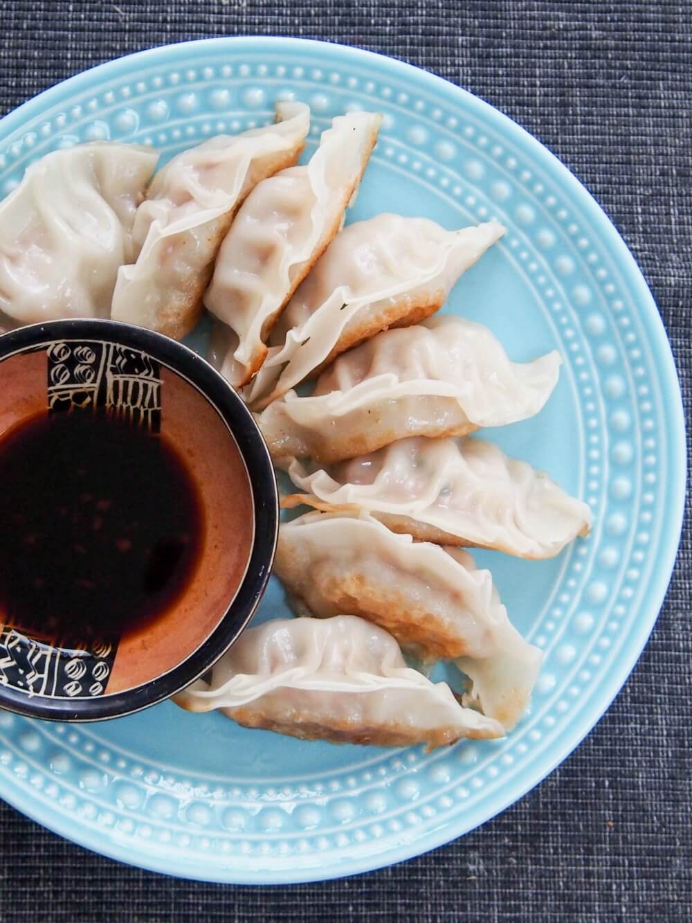 Pork and cabbage dumplings are a traditional dish eaten for Chinese New Year, but these dumplings are so delicious you'll want to have them more often! Chinese pork and cabbage dumplings on plate with dipping sauce in small bowl to side