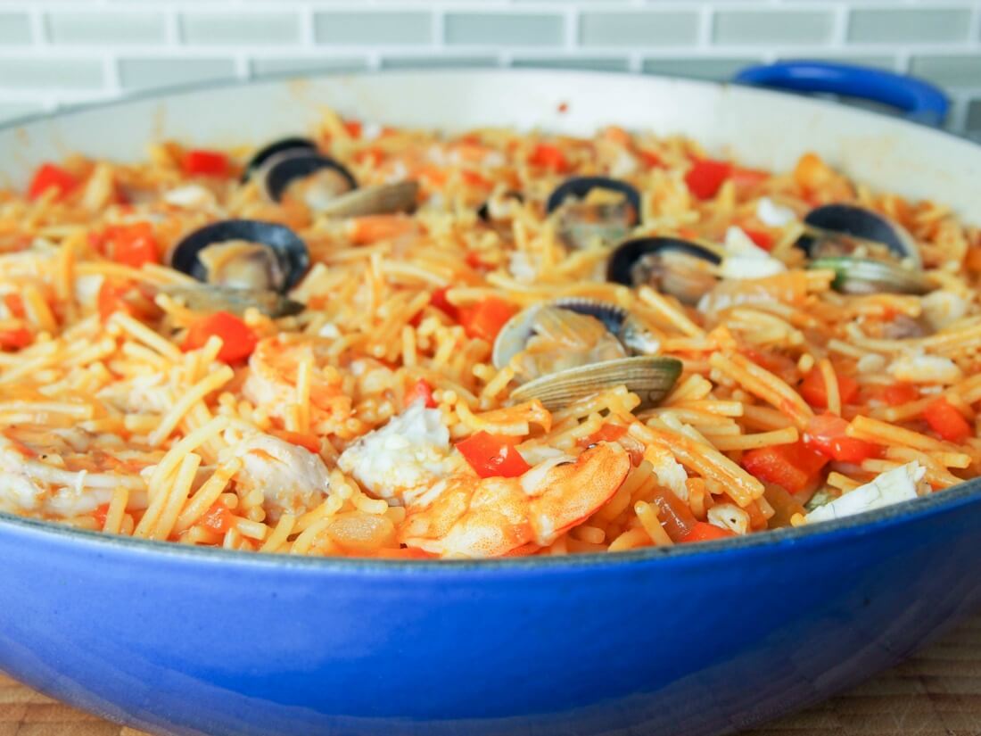 Fideua is a Catalan fish and seafood paella made with short pasta and a tomato-pepper and stock sauce base. Deliciously comforting. fideua (Catalan pasta paella) in pan from side
