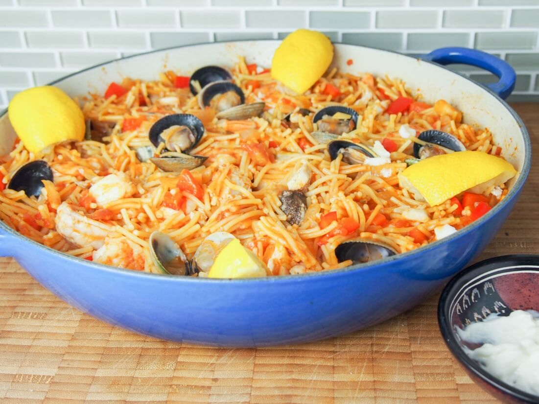 fideua (Catalan pasta paella) in pan with lemon slices around side