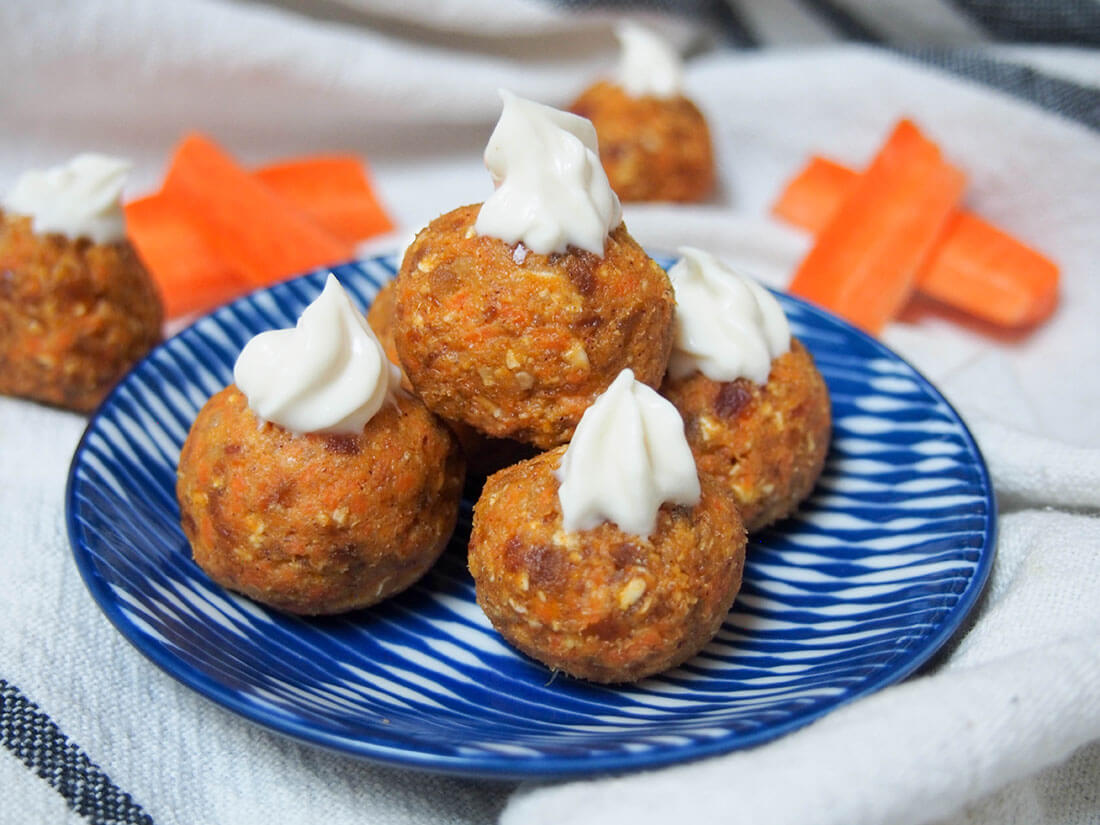 carrot cake energy bites stacked on a small plate with carrot slices behind