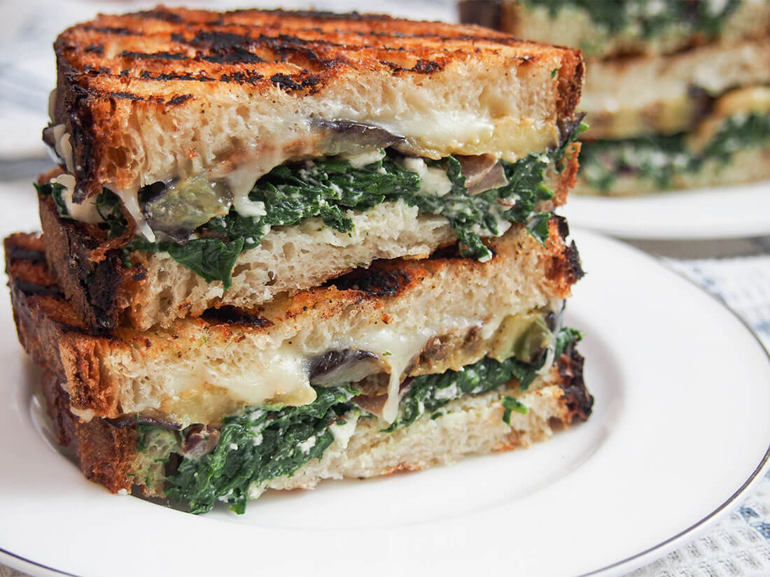 This eggplant spinach grilled cheese sandwich draws on Greek flavors for a deliciously cheesy vegetarian grilled cheese. It's hearty and filling, but without feeling too heavy since it's veggie-packed too! Eggplant spinach grilled cheese sandwich on plate with another behind