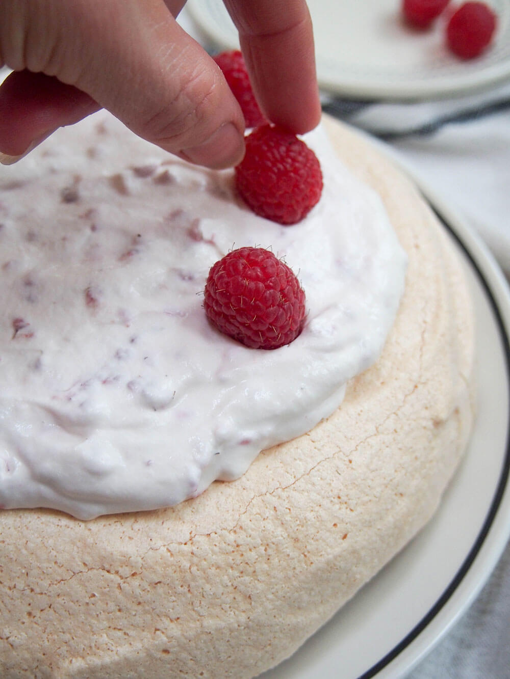 decorating pavlova with raspberries and cream