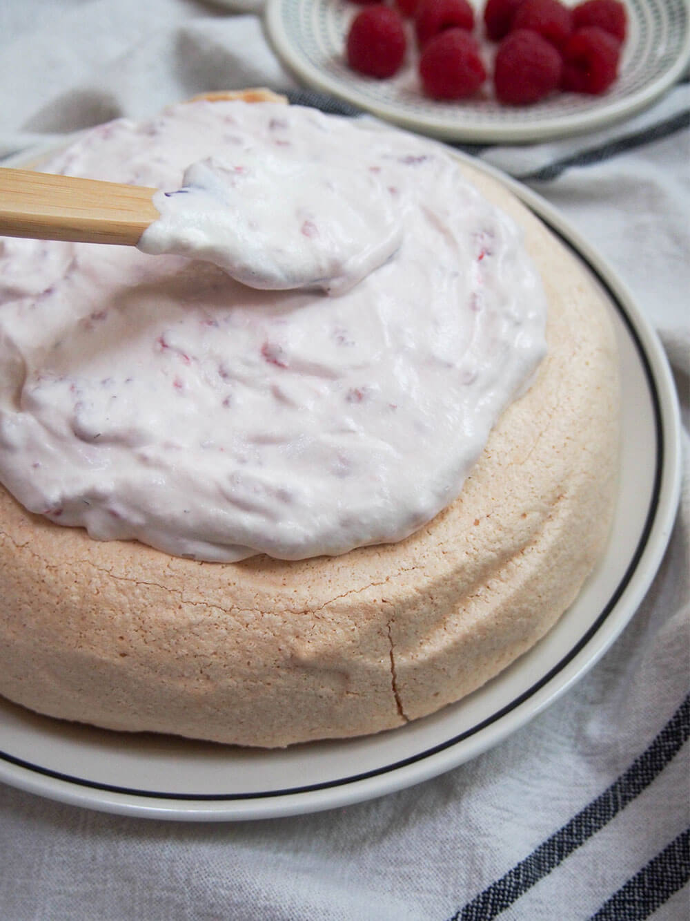 adding cream to pavlova with raspberries and cream