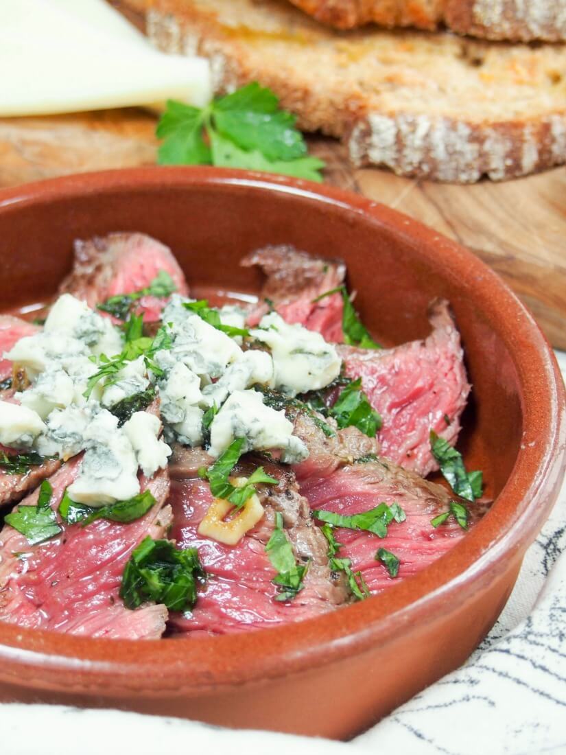 Side view of slices of steak topped with blue cheese in red ceramic dish