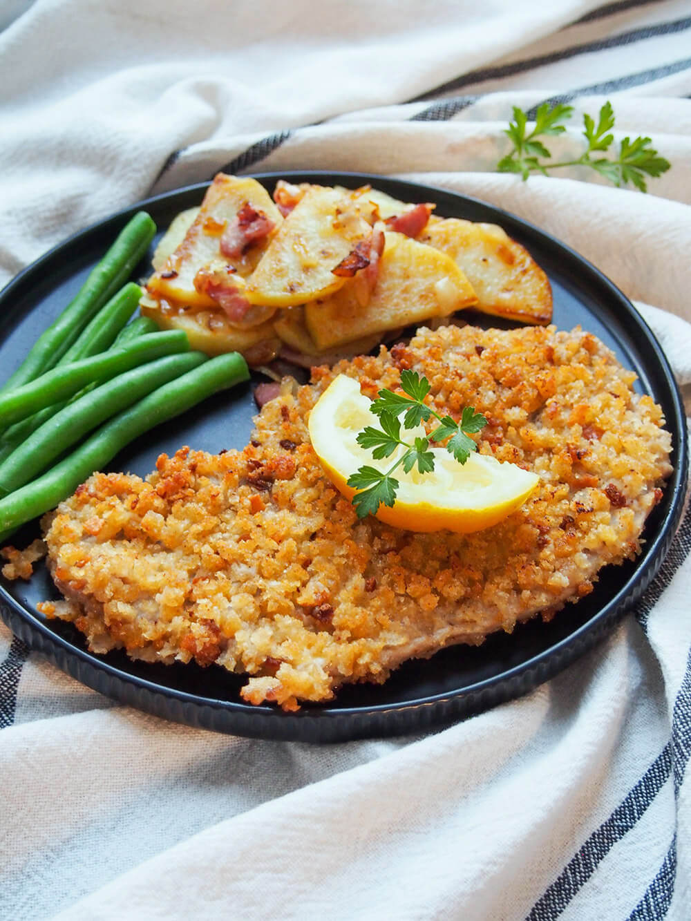 Wiener schnitzel topped with slice of lemon with sides of beans and potatoes to side