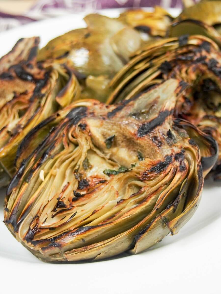 close up view of a half grilled artichoke with more behind