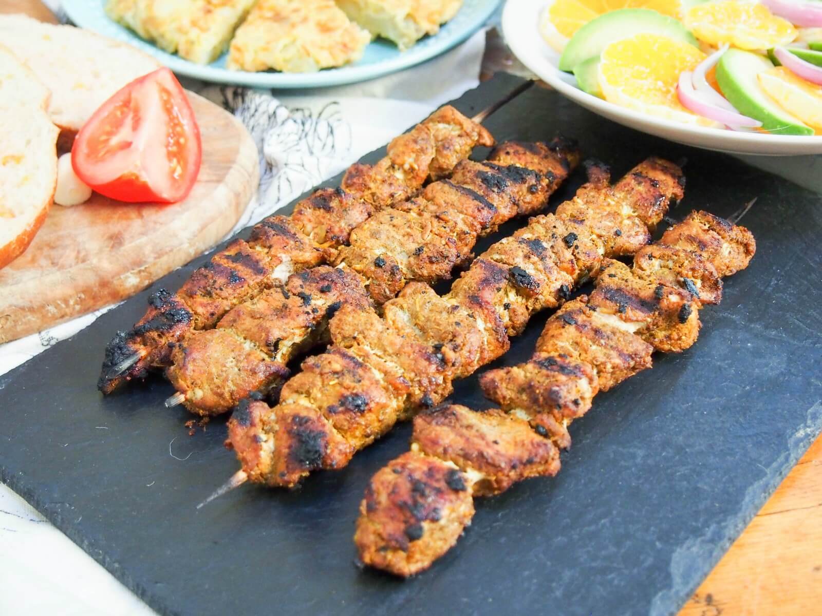 Pinchos morunos are Spanish pork skewers with an aromatic spice marinade. They're easy to make, full of flavor and the perfect tapas dish to add to your next party or get-together. pinchos morunos on slate with tortilla behind and plate of salad