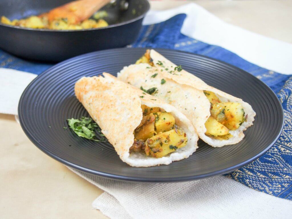 masala dosa on plate with extra filling in skillet behind