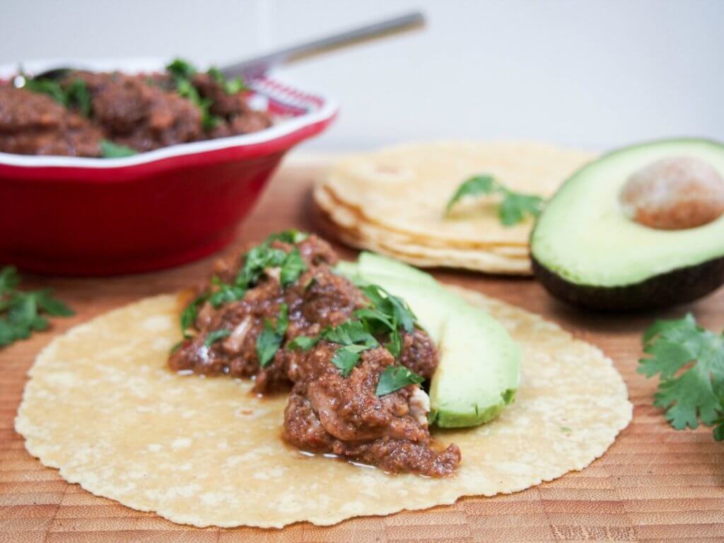 chicken mole on tortilla with avocado to one side and bowl with additional chicken behind