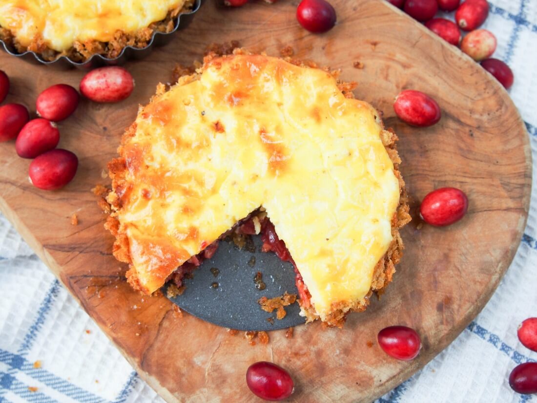 savory cranberry and cheese tart with piece cut out of it and cranberries around tart