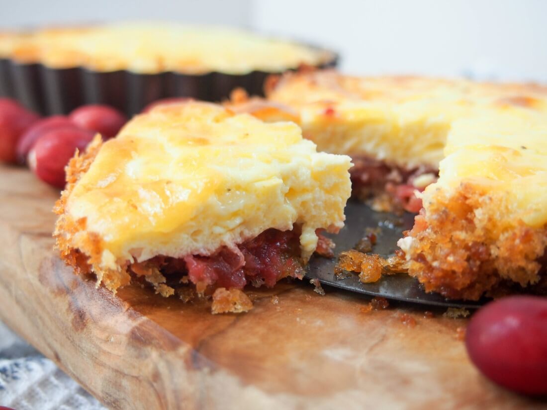 piece of tart cut from rest showing layers of cheese topping, cranberries and base