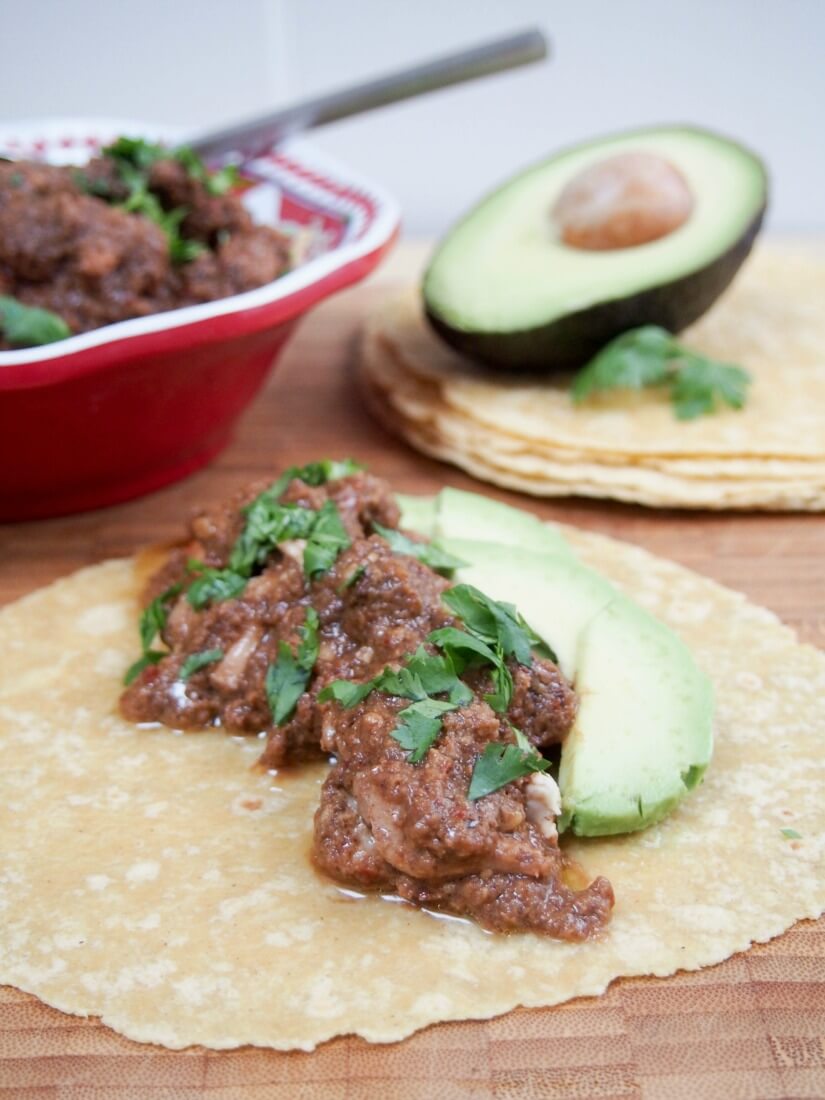 slow cooker chicken mole on tortilla along with slices of avocado
