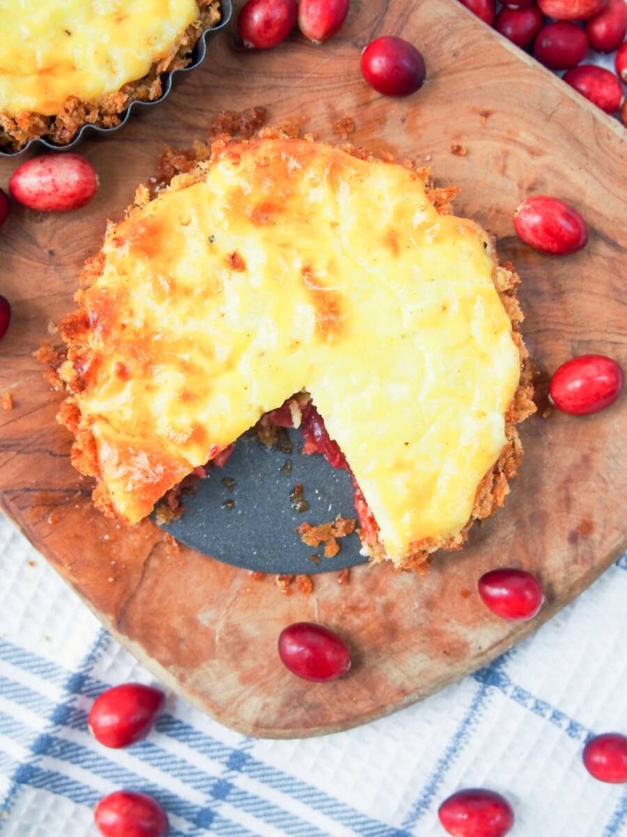 Savory cranberry and cheese tart on wooden board with slice cut from it viewed from oerhead
