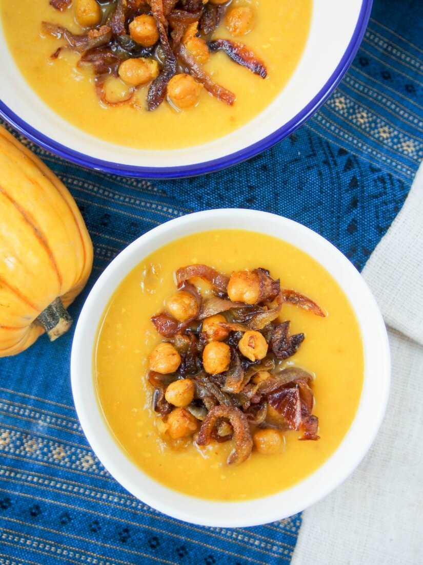 Two bowls of delicata squash soup topped with curried chickpeas and onions viewed from overhead