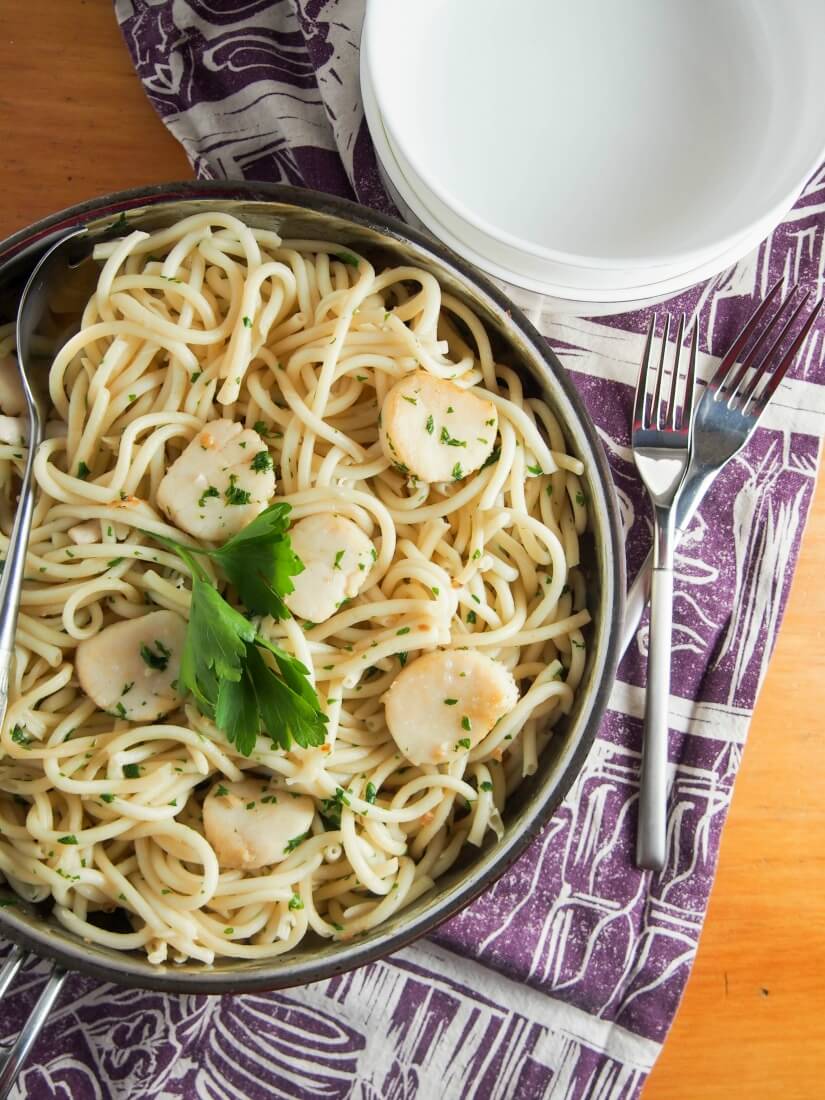 skillet with scallop pasta with garlic and white wine from overhead with bowls and forks to side of skillet