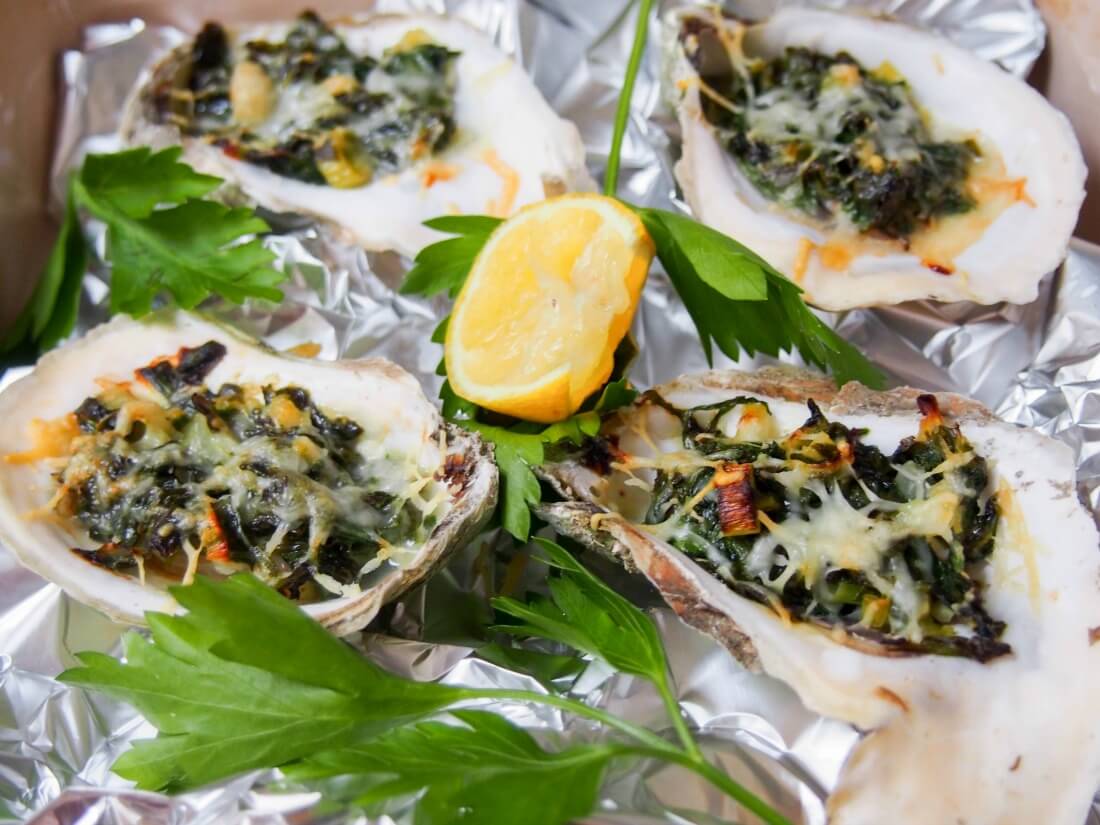 oysters Rockefeller on foil in baking dish with parsley and lemon garnishes