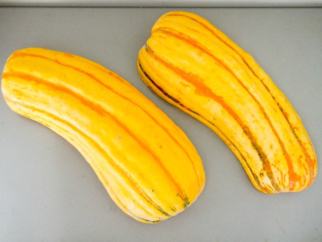 delicata squash split down middle and halves flat on baking sheet, ready to roast