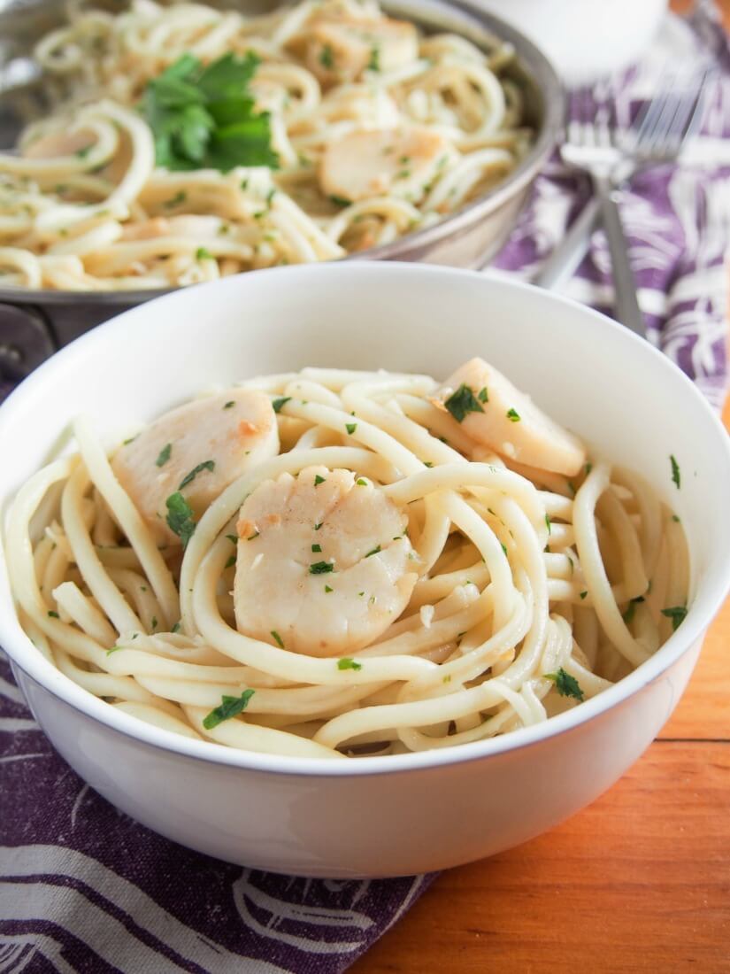bowl of scallop pasta with garlic and white wine with skillet behind