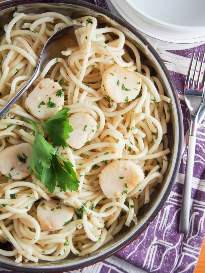 scallop pasta with garlic and white wine in skillet, topped with sprig of parsley