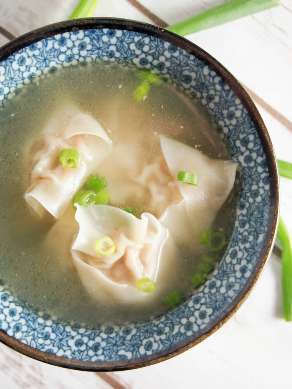 wontons in soup with slices of spring onion as garnish from overhead