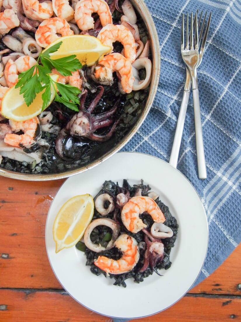 Spanish black rice paella (arroz nego/arròs negre) gets it's vibrant color from squid ink, but the flavor is delicate. Packed with seafood, it's a delicious meal. arroz nego/arròs negre with some served on small plate and rest in skillet and forks to side