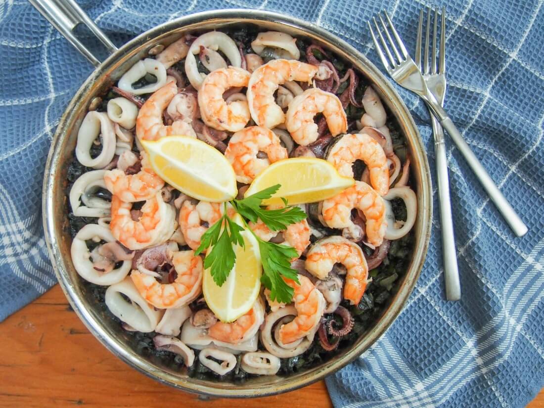 Spanish black rice paella (arroz nego/arròs negre) gets it's vibrant color from squid ink, but the flavor is delicate. Packed with seafood, it's a delicious meal. arroz negro - Spanish black rice paella - in skillet with forks to side