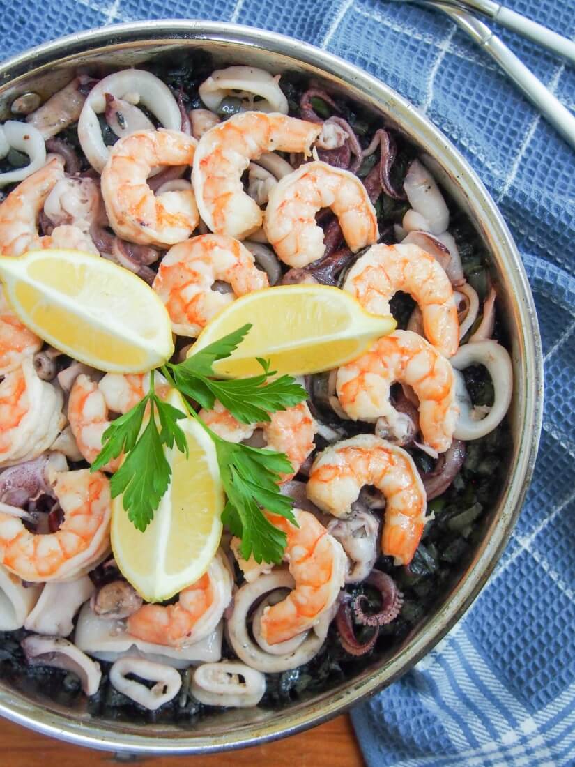Spanish black rice paella (arroz nego/arròs negre) gets it's vibrant color from squid ink, but the flavor is delicate. Packed with seafood, it's a delicious meal. Spanish black rice paella in skillet from overhead, topped with slices of lemon