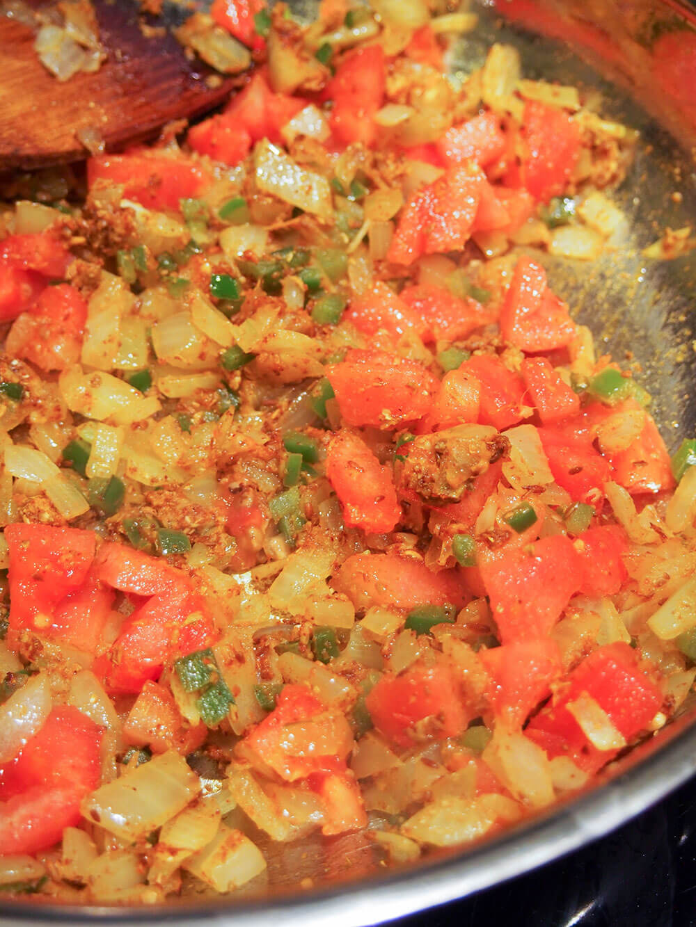 adding tomatoes to onion and spice base for sauce