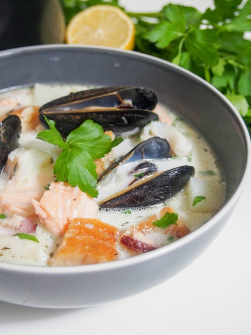bowl of Irish fish chowder from side with parsley and lemon behind
