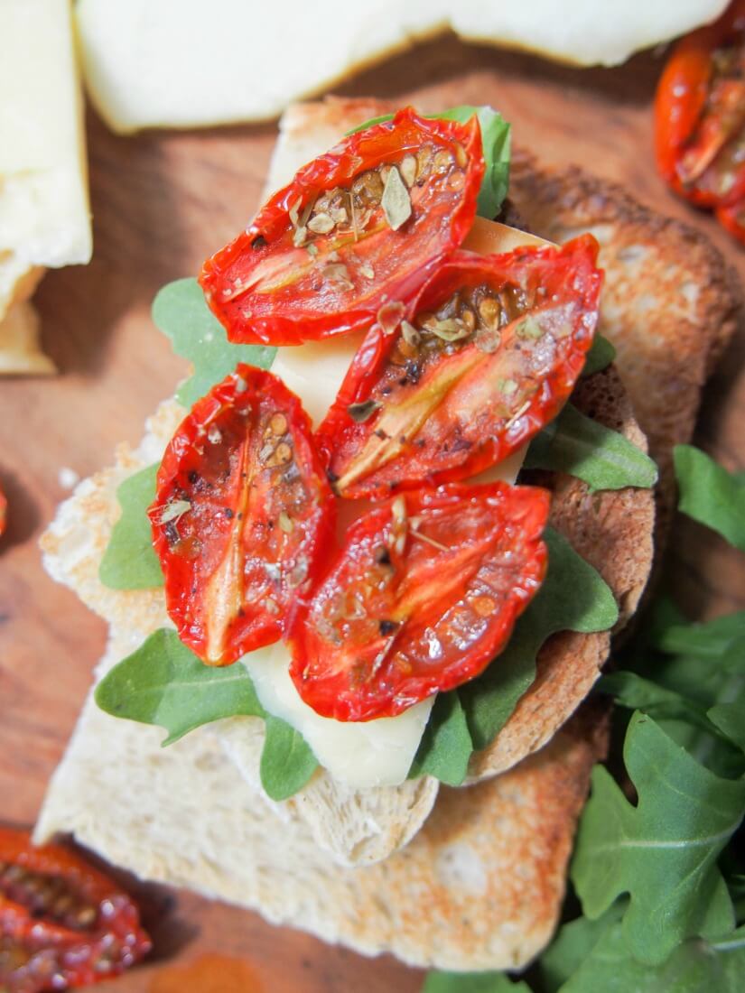 slow roasted tomatoes on top of cheese and arugula toast from above