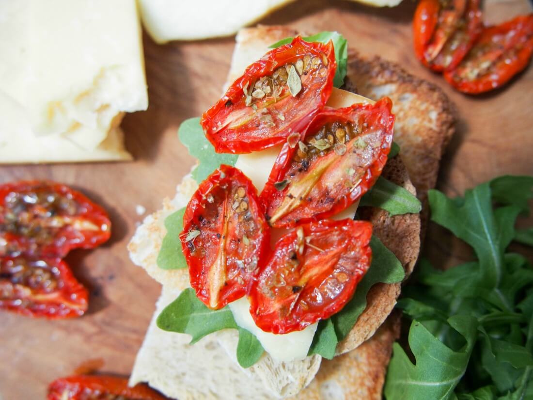 slow roasted tomatoes on top of cheese and arugula on toast
