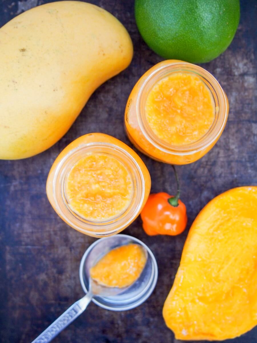 Mango habanero sauce gives a wonderful sweet-spicy kick to tacos and more. Really easy to make, and surprisingly healthy, it'll be a go-to hot sauce. jars of mango habanero sauce from above with mangoes to side and pepper by jar