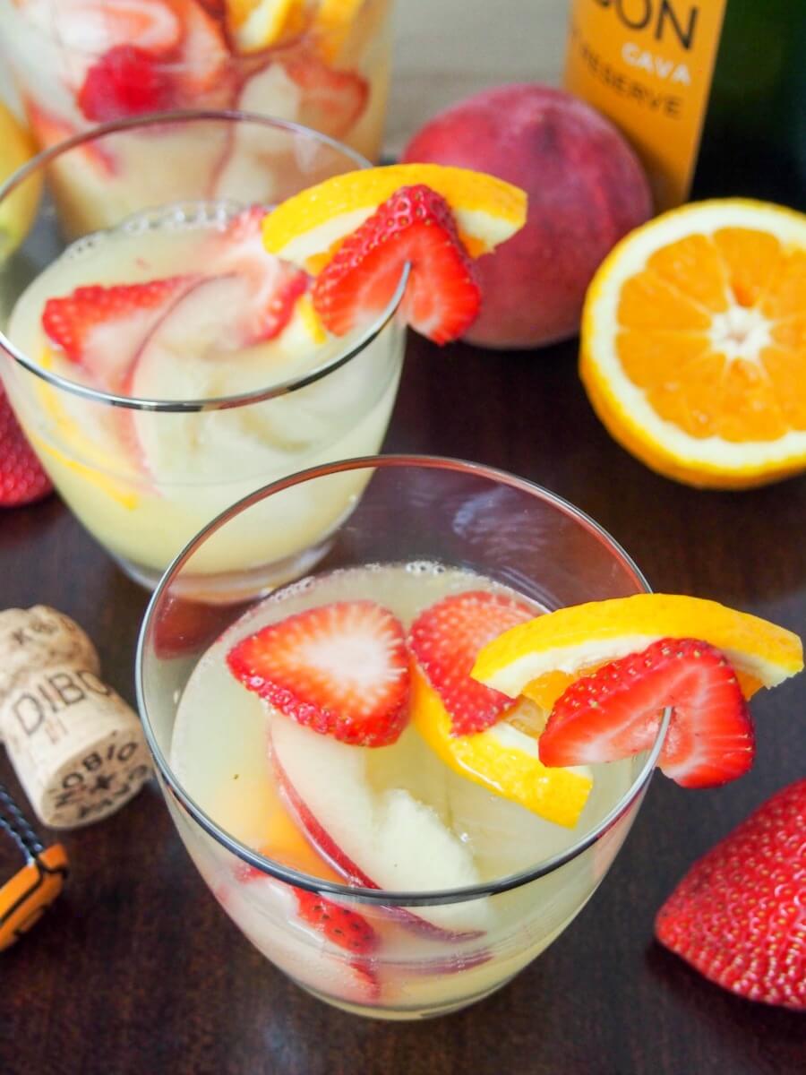 cava sangria is a bright and bubbly cocktail perfect any excuse two glasses of cava sangia with fruit behind and cork to side