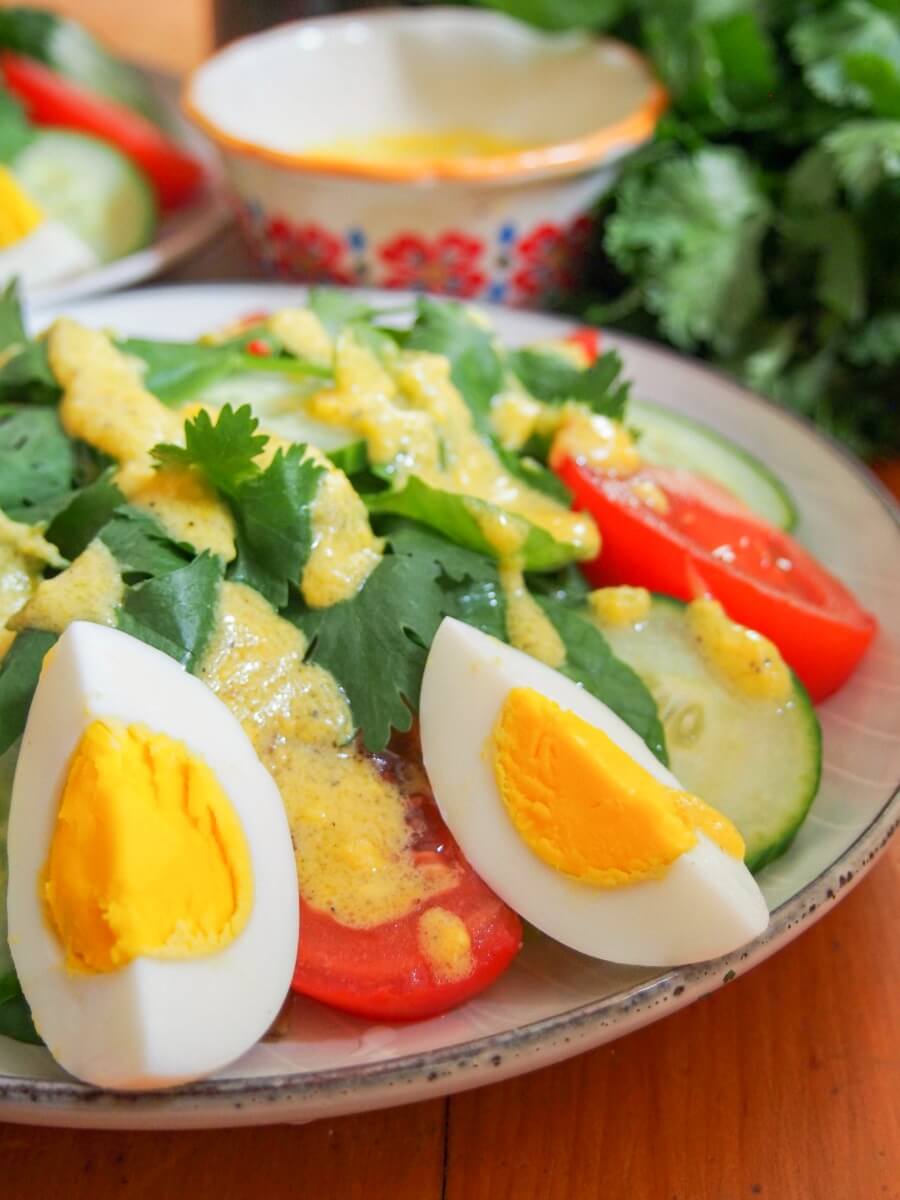 close up of Laos salad showing hard boiled egg, tomato and cucumber on top of greens
