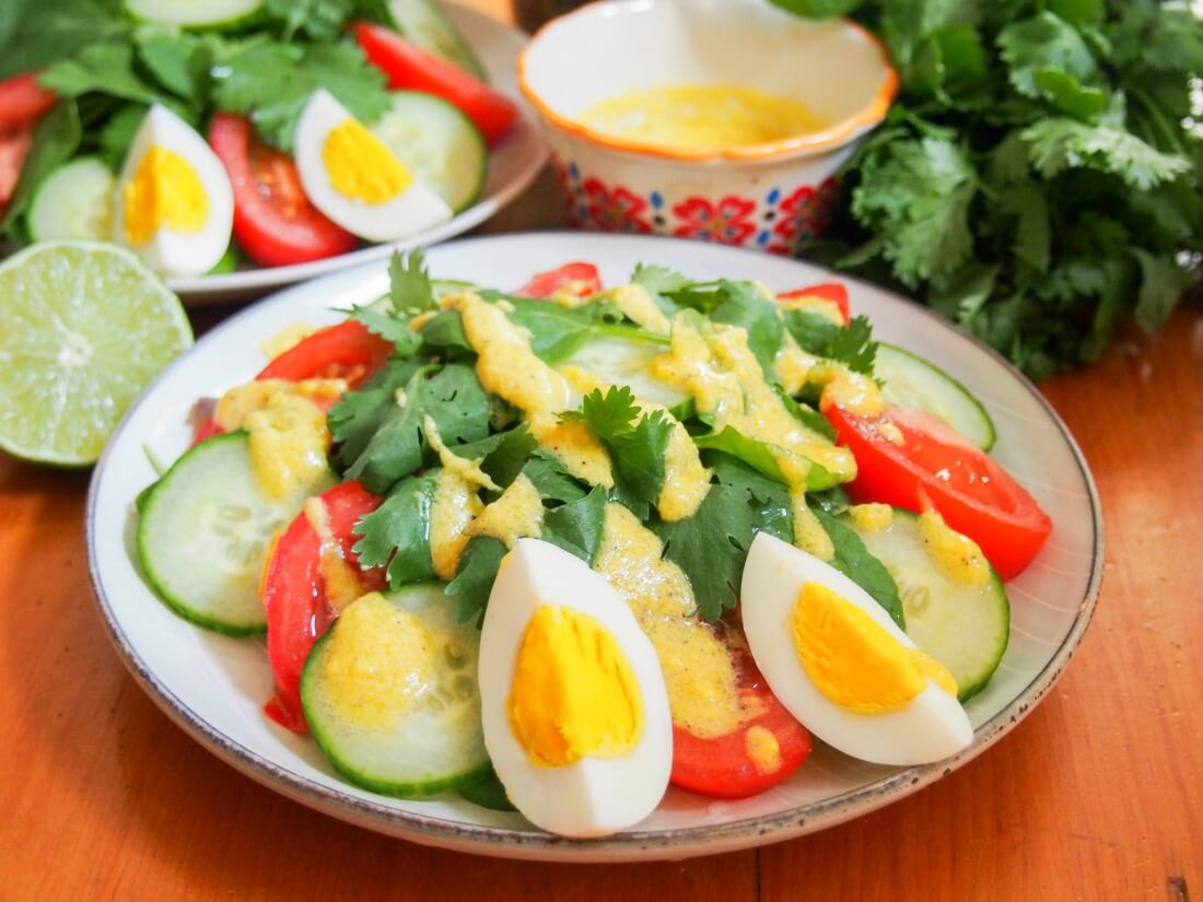 plate of Luang Prabang salad with dressing drizzled over top and extra dressing and cilantro behind