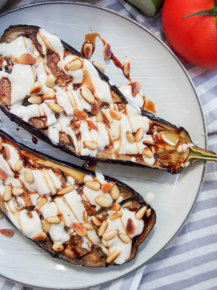 Roasted eggplant with tahini drizzled on top and pine nuts, viewed from overhead