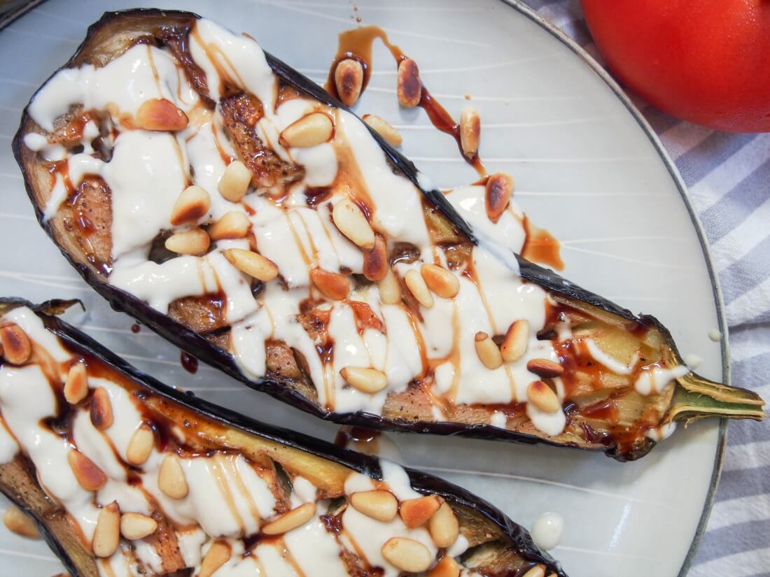 Roasted eggplant with tahini is a delicious appetizer or mezze dish that you'll find in Israel and other parts of the region. It's incredibly easy to make and full of fantastic flavor. One half of a roasted eggplant with tahini drizzle, other half partially in view