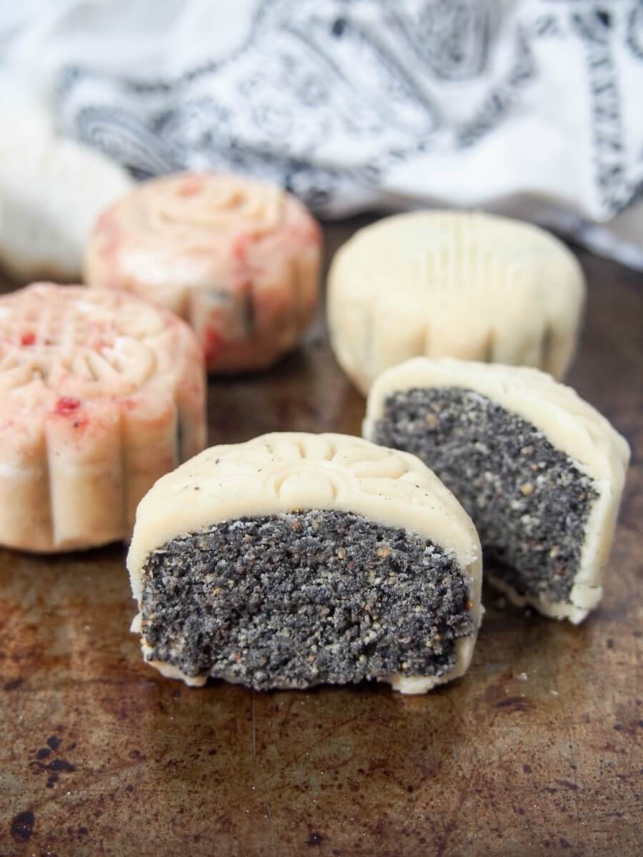cut Chinese snow skin mooncake showing sesame filling in front of other whole ones