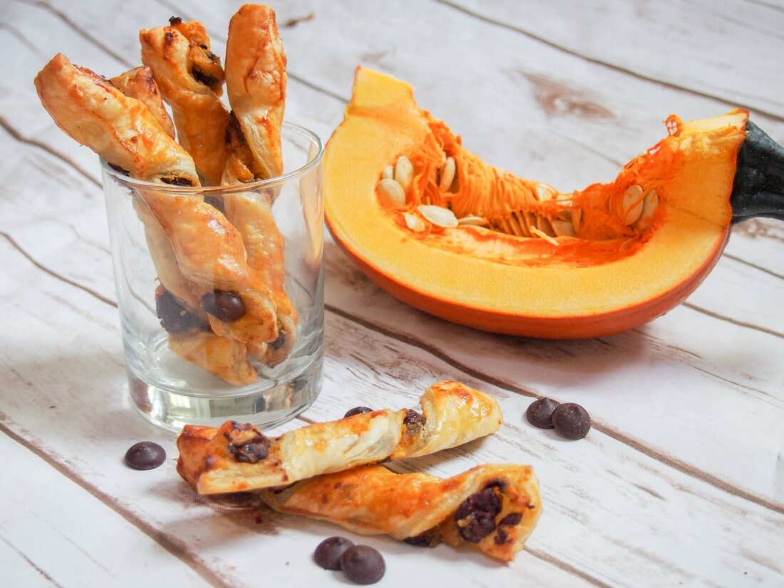 Whether you're a pumpkin fan or not, these chocolate pumpkin pastry twists are sure to be a hit. A deliciously simple combination with a bit of sweet, a bit of spice, crisp pastry and soft filling. Chocolate pumpkin pastry twists in glass and some in front with chunk of pumpkin behind