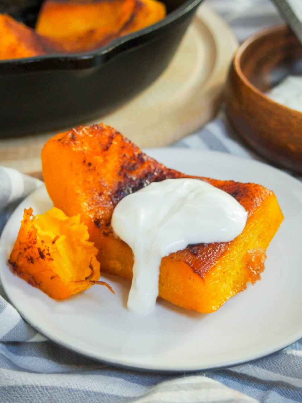 Kaddo bowrani (Afghan pumpkin with yoghurt sauce) on small plate with skillet behind
