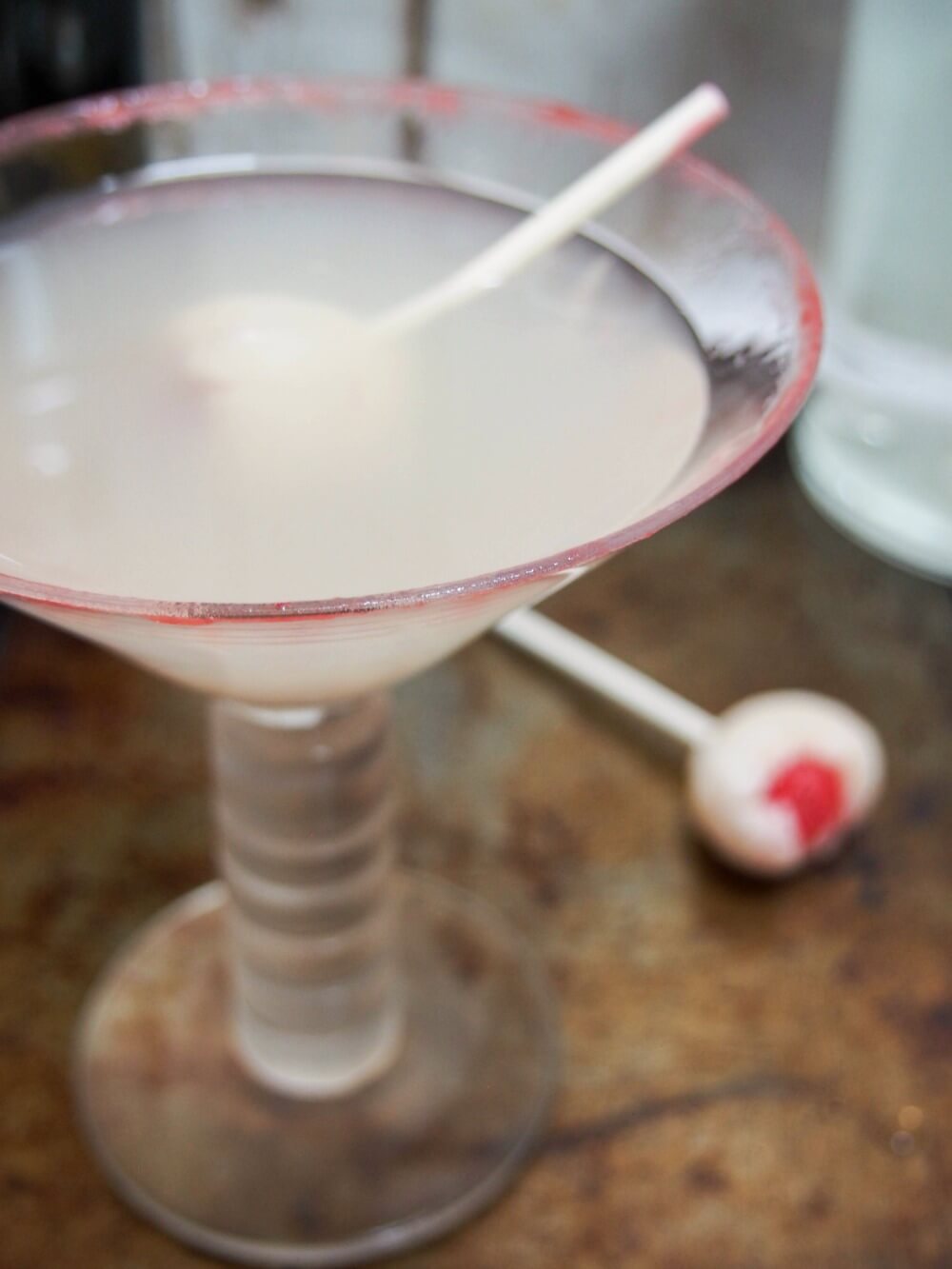 lychee martini in glass with lychee raspberry 'eyeball' stirrer behind