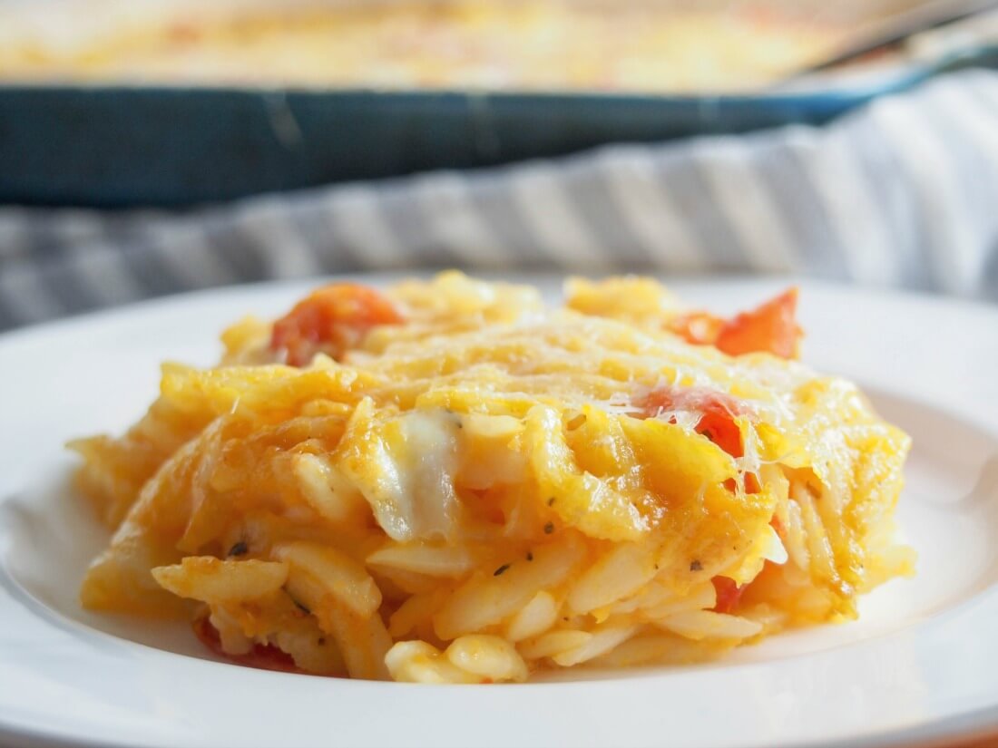 This cheesy orzo pasta bake is comfort food on a plate, with a slightly healthy twist. With lots of cheese and veggies, it's a great vegetarian meal. serving of cheesy orzo pasta bake on plate