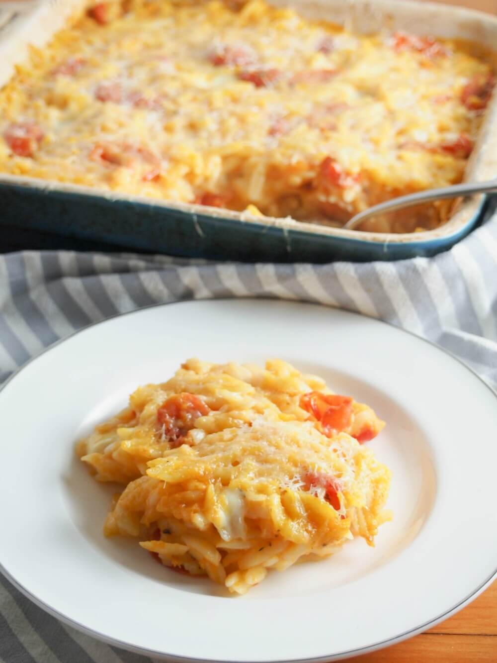 This cheesy orzo pasta bake is comfort food on a plate, with a slightly healthy twist. With lots of cheese and veggies, it's a great vegetarian meal. Cheesy orzo pasta bake on plate with baking dish with more behind