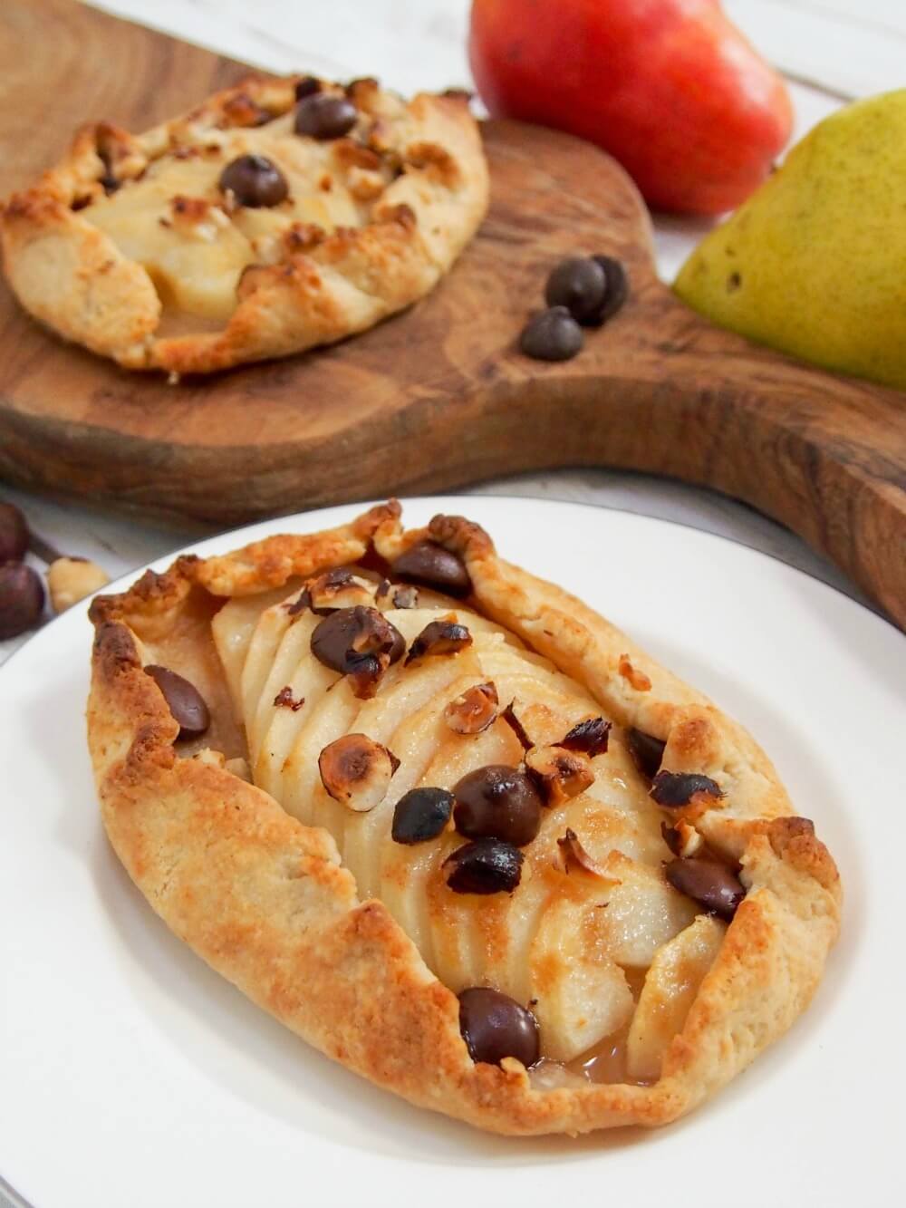 Individual pear galette on plate with another behind on wooden board