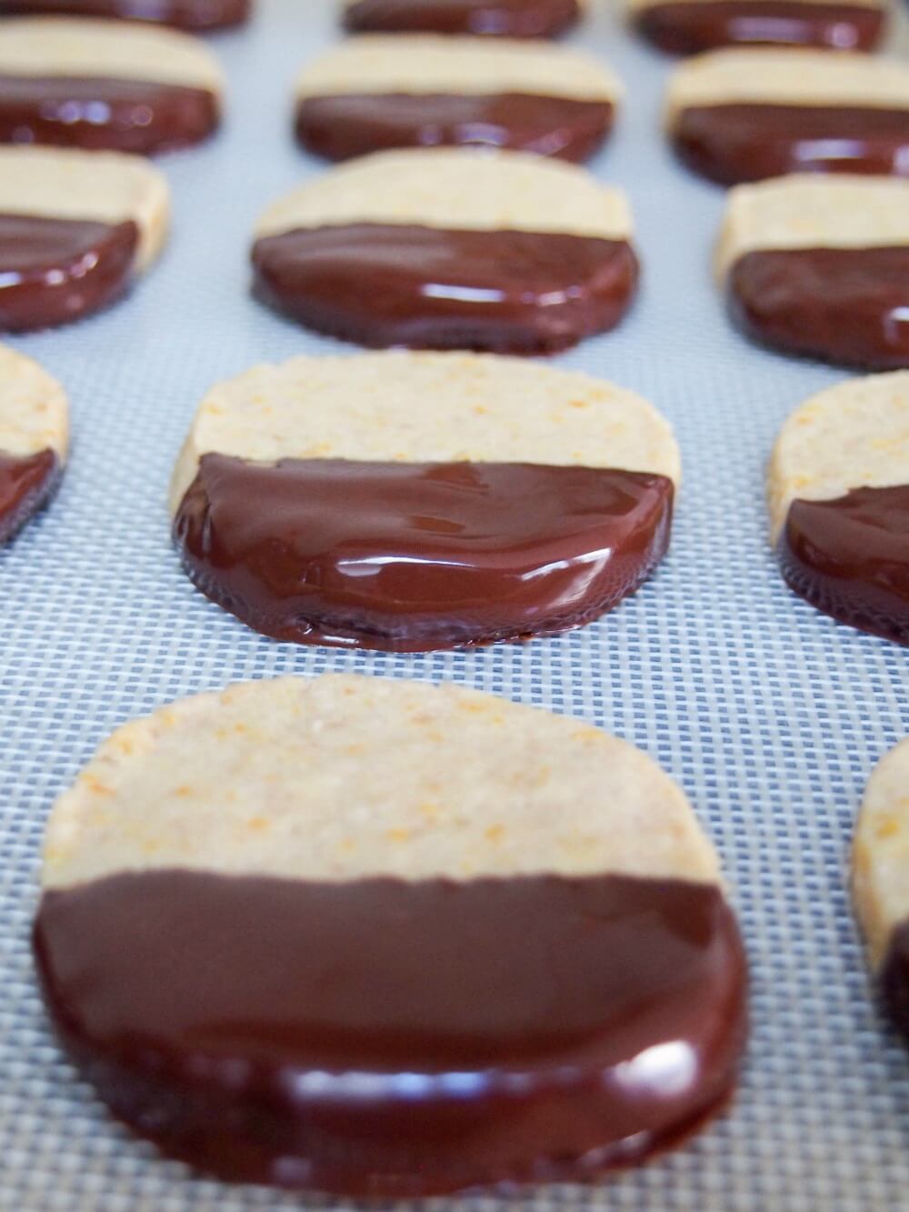 orange shortbread cookies dipped in chocolate drying on mat