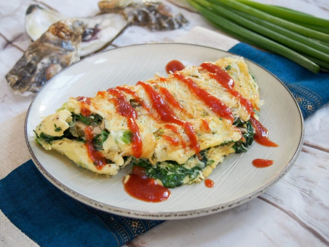 Taiwanese oyster omelette is a classic street food, but it also makes a delicious brunch/lunch - easy to make and with lots of great flavor, with oysters, greens and a flavorful sauce. Taiwanese oyster omelette on plate with oyster shells and scallions behind