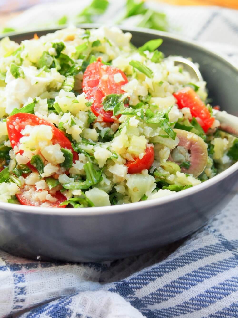 bowl of cauliflower rice salad showing pieces of tomato and olives mixed in
