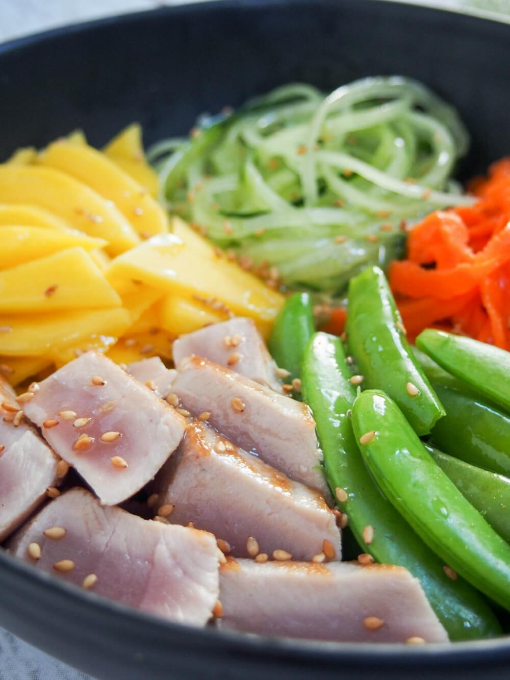 close up from side of seared tuna and veggie bowl showing sesame dressing on top