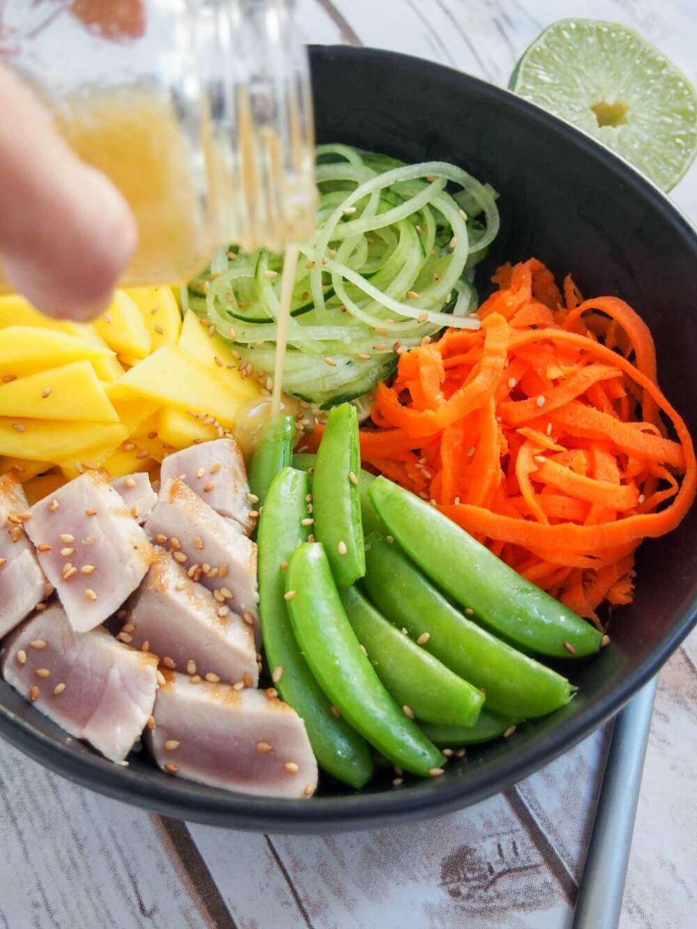 adding dressing to seared tuna and veggie bowl